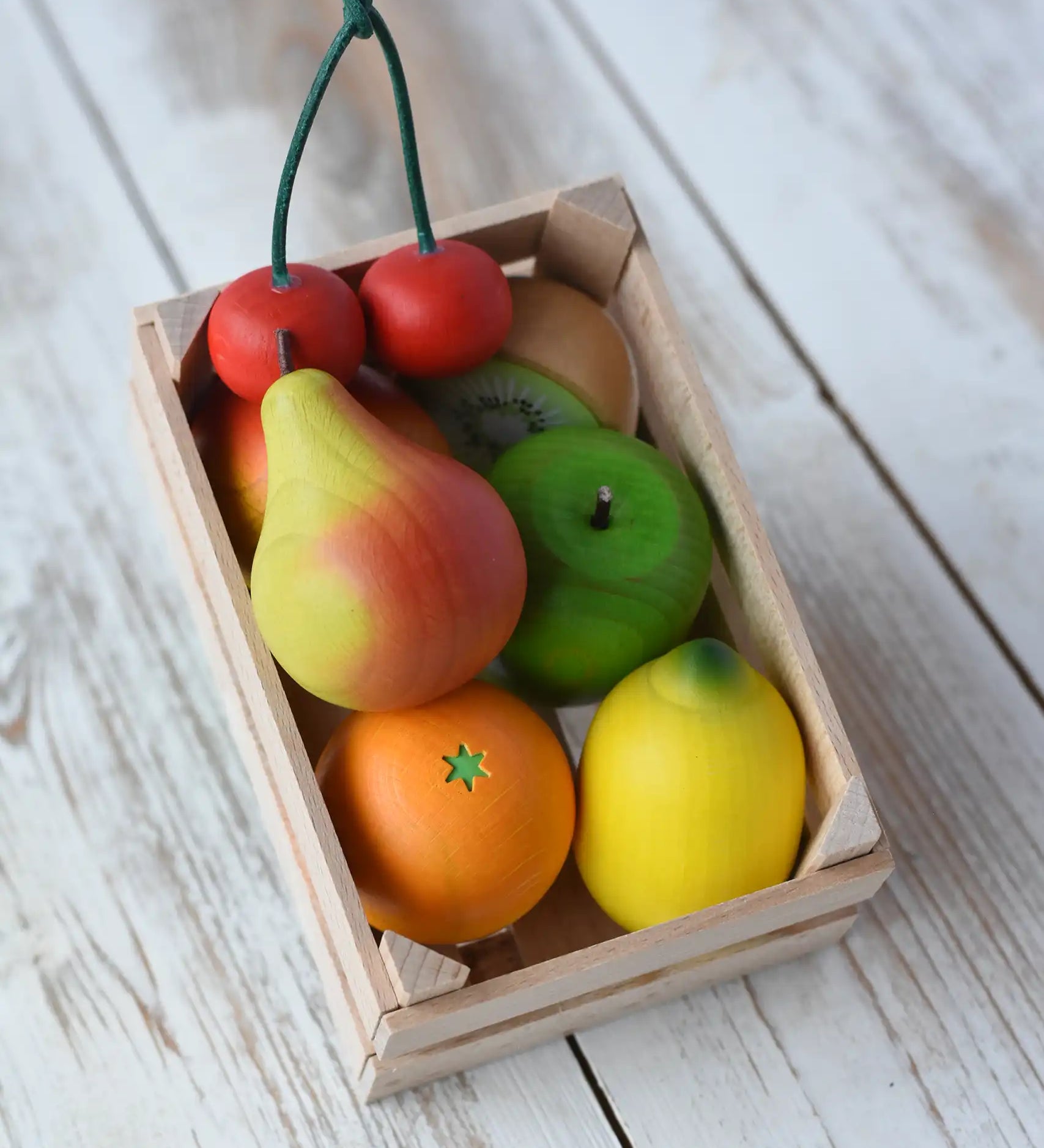 Erzi small wooden toy crate filled with wooden play food fruits placed on a wooden surface. 