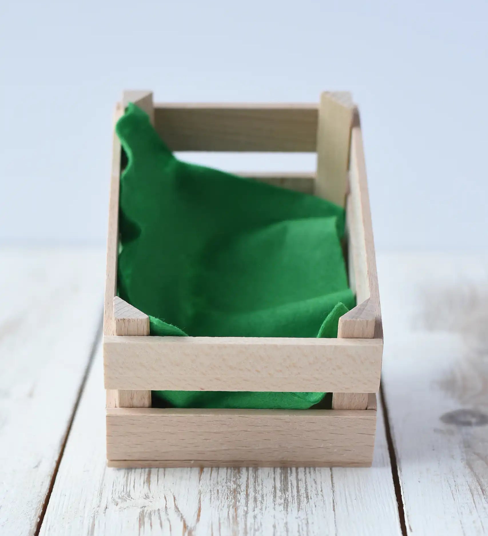 Erzi small wooden toy crate placed on a wooden surface with a piece of green felt inside.  