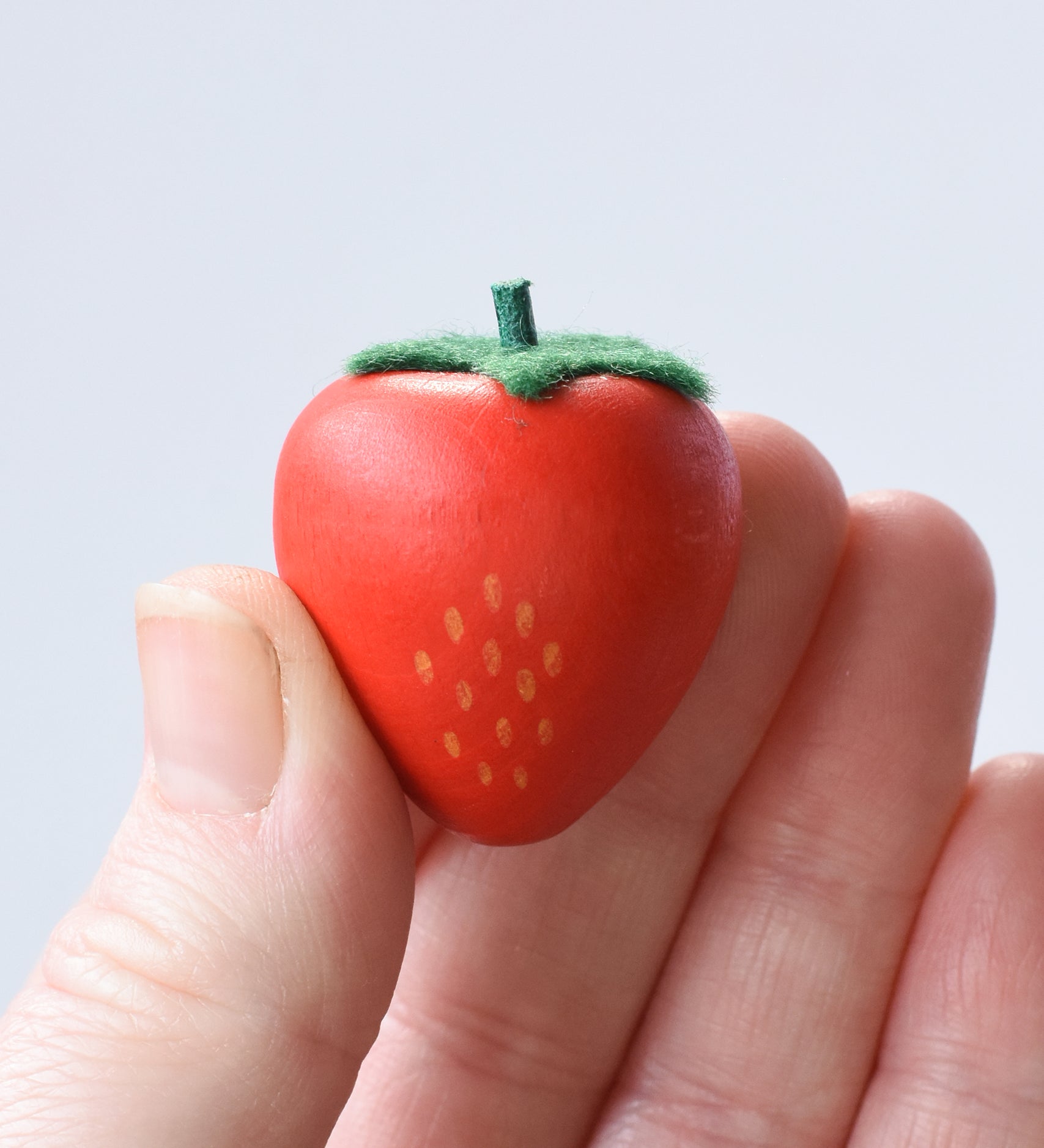 Erzi small red strawberry wooden play food in an adult's hand.