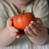 An Erxi wooden toy pumpkin in a child's hand. 