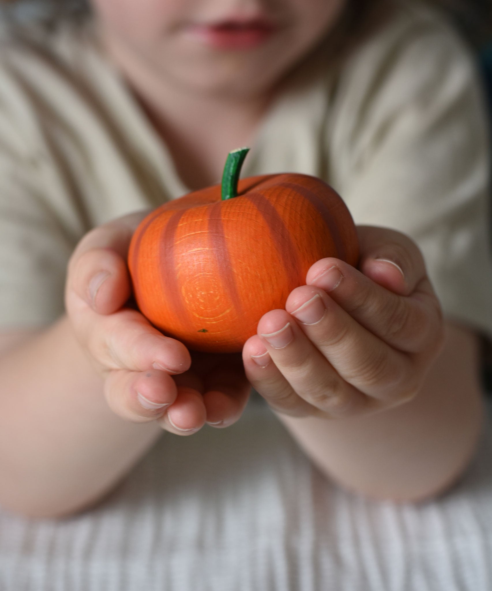 An Erxi wooden toy pumpkin in a child's hand. 