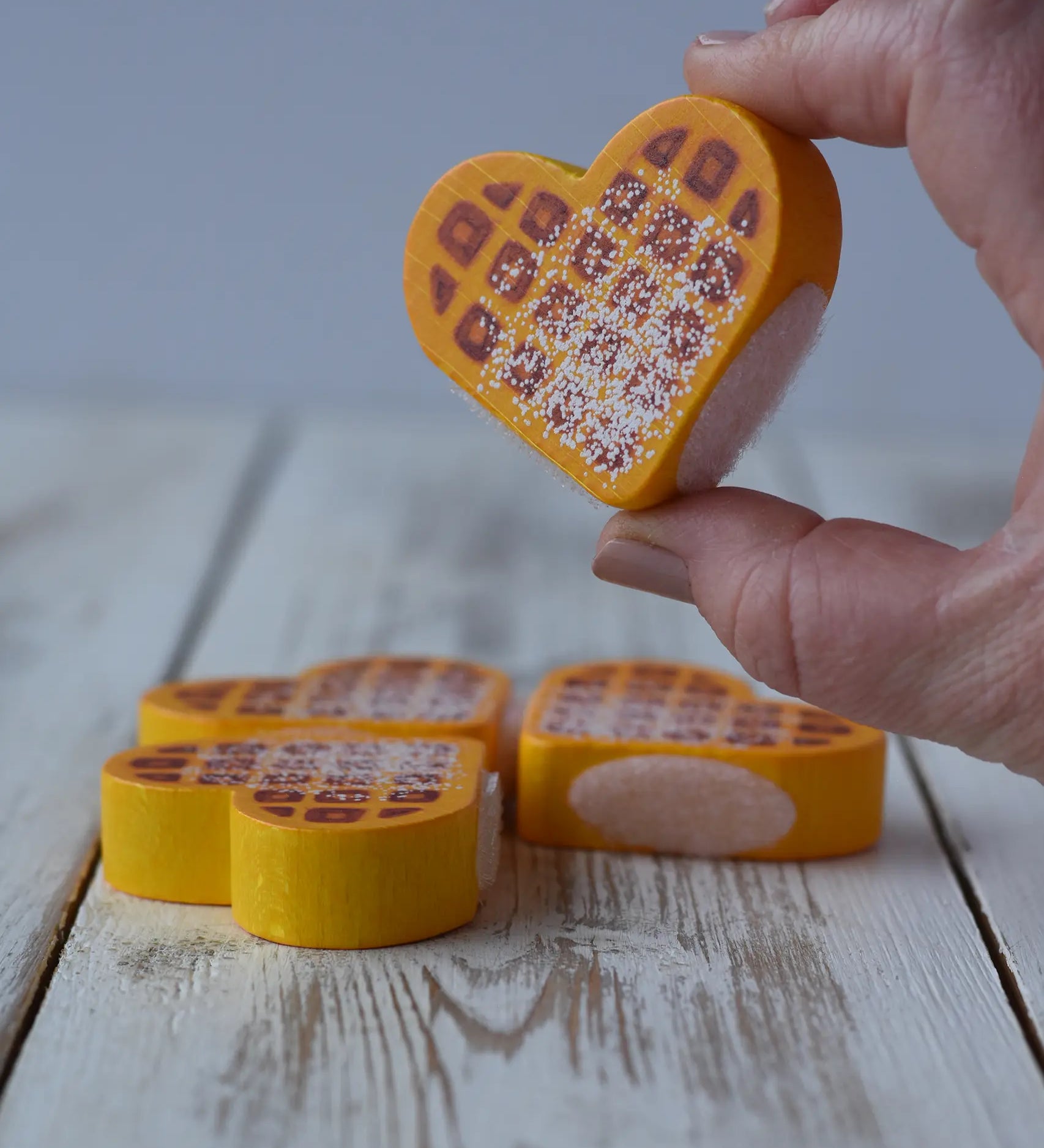 Heart shaped piece of waffle from the Erzi Waffles To Cut Wooden Play Food in an adult's hand.