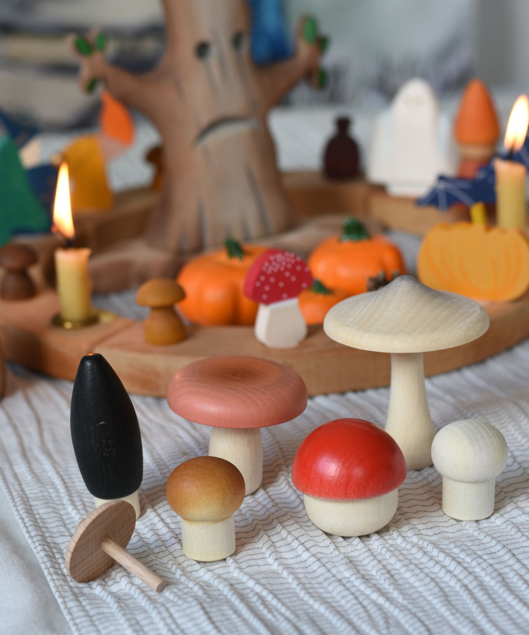 A selection of the wooden mushrooms from the Erzi Forest mushrooms in a box set placed on a striped tablecloth in front of an Autumnal themed Grimm's celebration ring set up. 