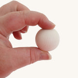 A close up of a Erzi 300 white wooden marble in an adult's hand, they are holding it up by a thumb and finger to show scale.