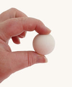 A close up of a Erzi 300 white wooden marble in an adult's hand, they are holding it up by a thumb and finger to show scale.