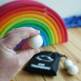 A close up of an Erzi 30mm marble in an adult's hand. A Grimm's rainbow can be seen blurred out in the background.  