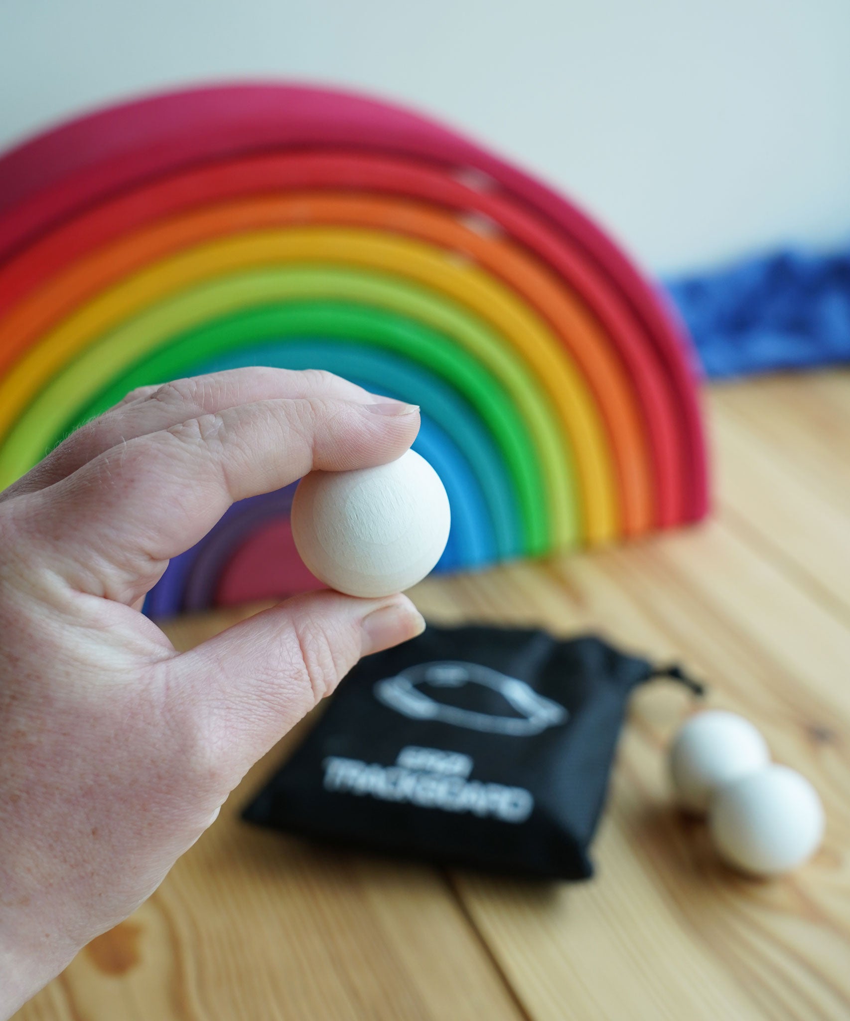 A close up of an Erzi 30mm marble in an adult's hand. A Grimm's rainbow can be seen blurred out in the background.  