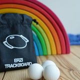 The set of three Erzi 30mm marbles placed on a wooden surface with a Grimm's rainbow in the background. The black drawstring storage bag that they come in can be seen in the background. 