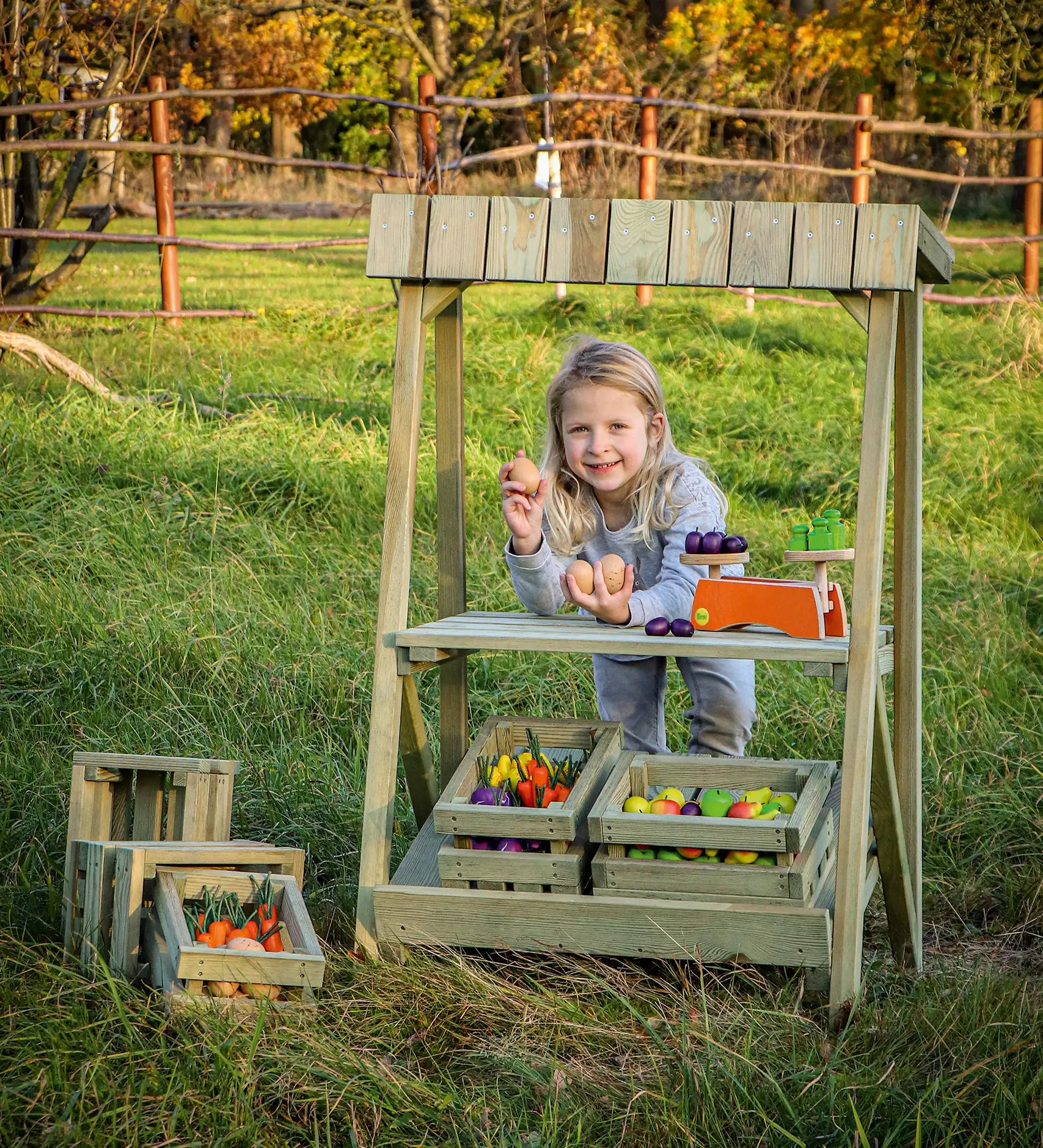 Child playing shop with the Erzi pine outdoor market stall. The wooden crates are filled with play food produce and Erzi scales are placed on the upper shelf.