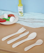 Erzi wooden toy cutlery set placed on a wooden surface in the Babipur playroom with wooden play food in the background.