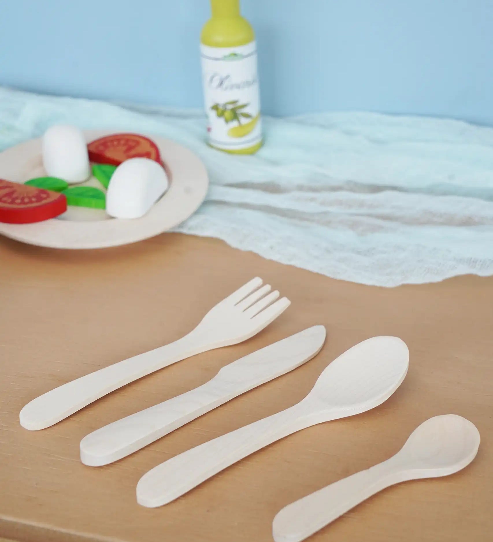 Erzi wooden toy cutlery set placed on a wooden surface in the Babipur playroom with wooden play food in the background.