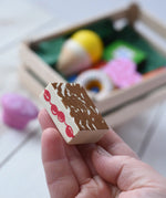 Cake from the Erzi assorted candies wooden play food set in an adult's hand. Wooden toy play food in a small wooden crate.
