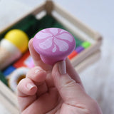 Pink cake from the Erzi assorted candies wooden play food set in an adult's hand. Wooden toy play food in a small wooden crate.