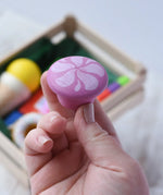 Pink cake from the Erzi assorted candies wooden play food set in an adult's hand. Wooden toy play food in a small wooden crate.