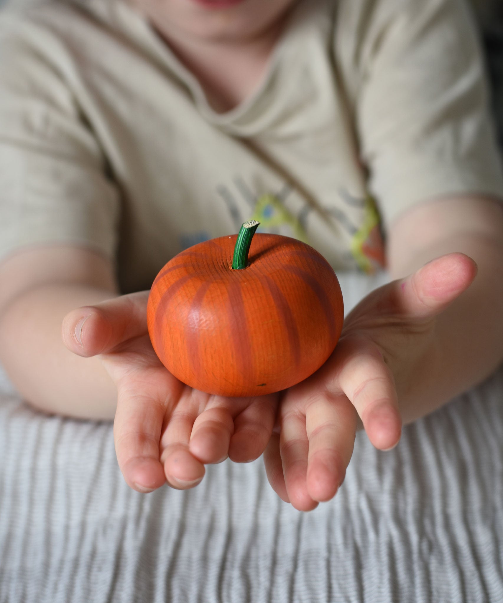 An Erzi wooden toy pumpkin in a child's hand.