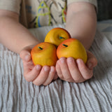 Three red Erzi apple playfood in a child's hands.
