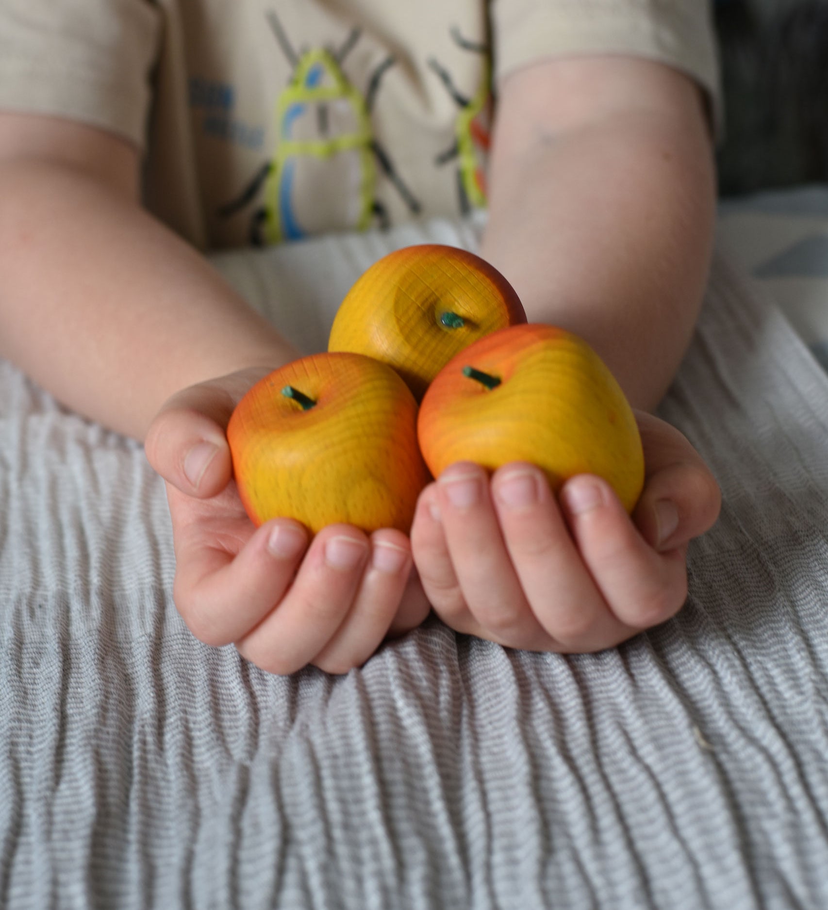 Three red Erzi apple playfood in a child's hands.