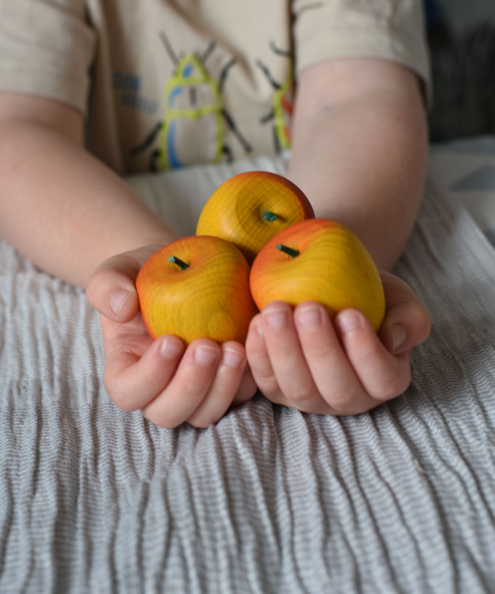 Three red Erzi apple playfood in a child's hands.