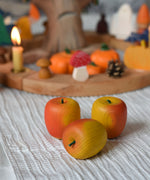 Three red Erzi wooden toy apples placed in front of an Autumnal themed celebration ring.