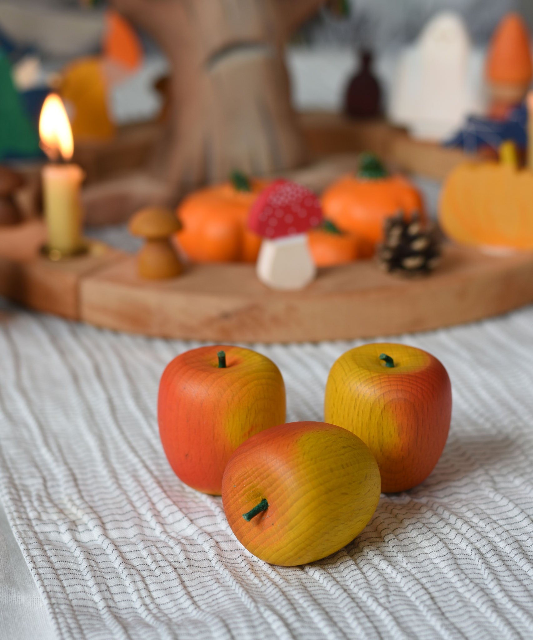 Three red Erzi wooden toy apples placed in front of an Autumnal themed celebration ring.