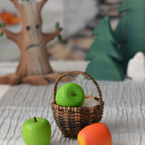 A green Erzi toy apple placed in a Kraul basket with a green and red apple placed besides it.