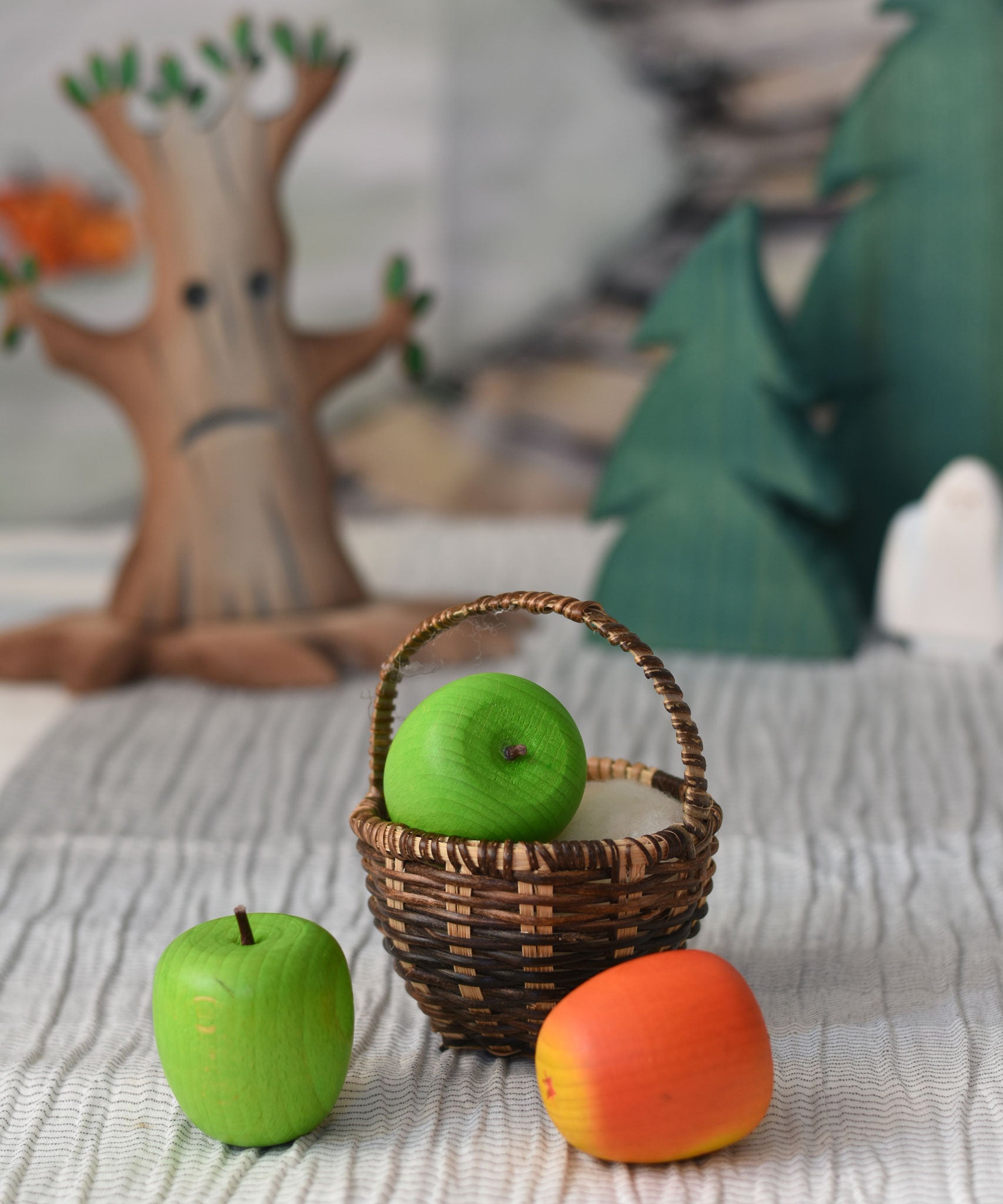 A green Erzi toy apple placed in a Kraul basket with a green and red apple placed besides it.