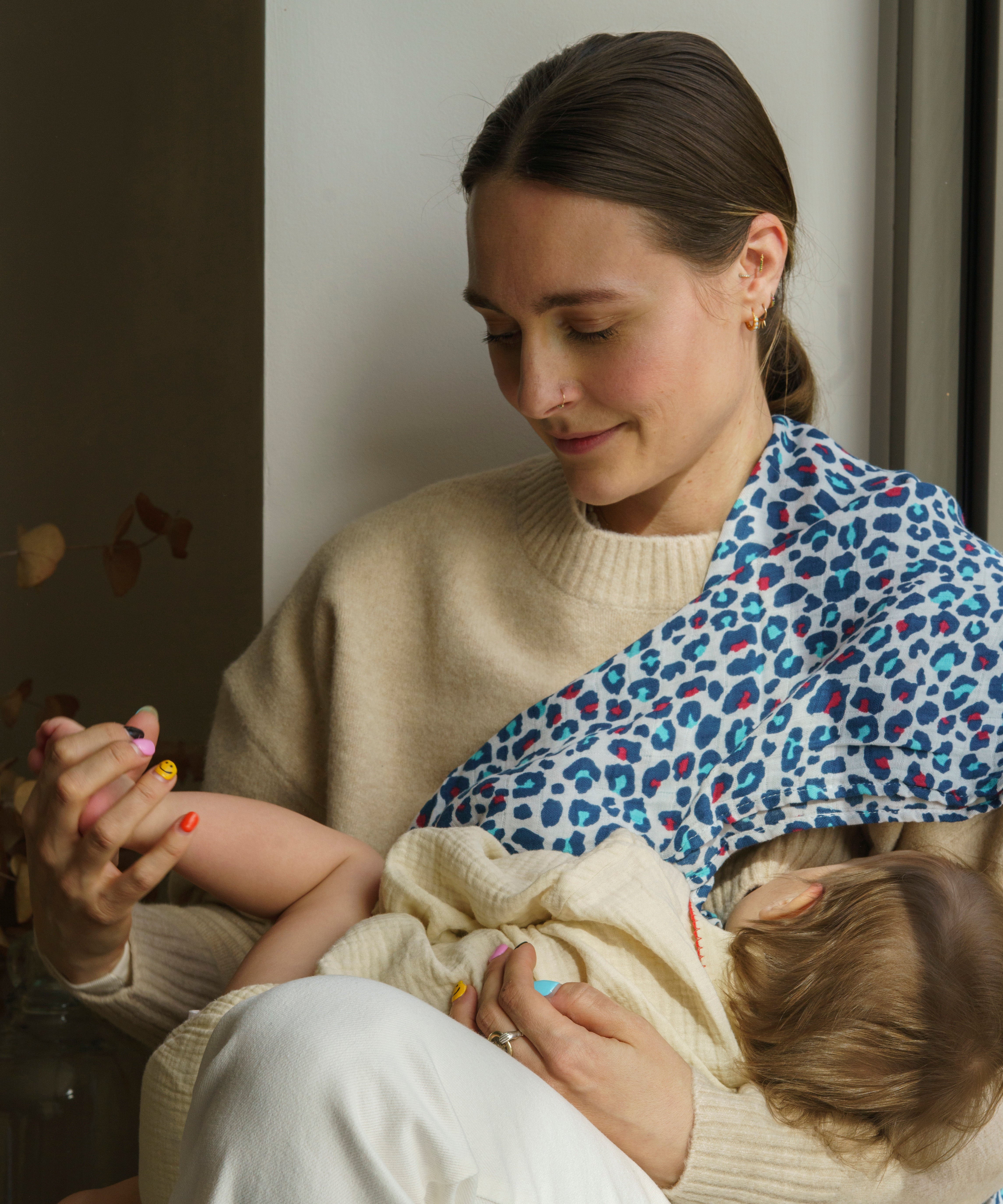 A mother holding a baby with the Etta Loves Extra Large Organic Cotton Baby Muslin Square - Blue Leopard on the shoulder
