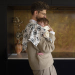 An adult holding a baby closely in a kitchen with the Etta loves XL dandelion muslin square on the shoulder
