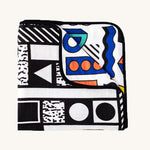 Etta Loves x Camille Walala Muslin Blanket folded into a square with one corner folded down showing the coloured side. 