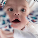 A baby looking wide-eyed at the Etta Loves organic cotton muslin square in an orange leopard print.