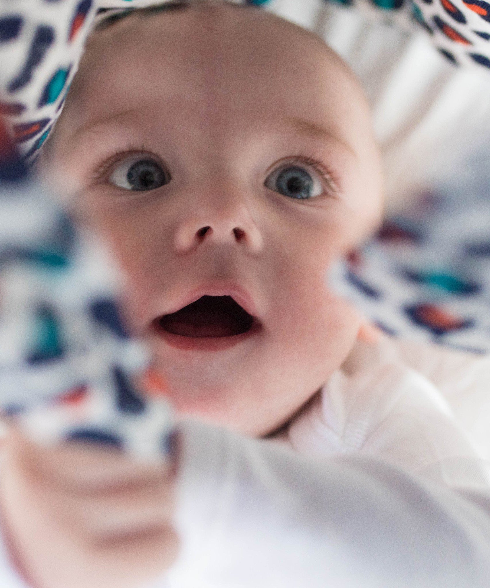 A baby looking wide-eyed at the Etta Loves organic cotton muslin square in an orange leopard print.