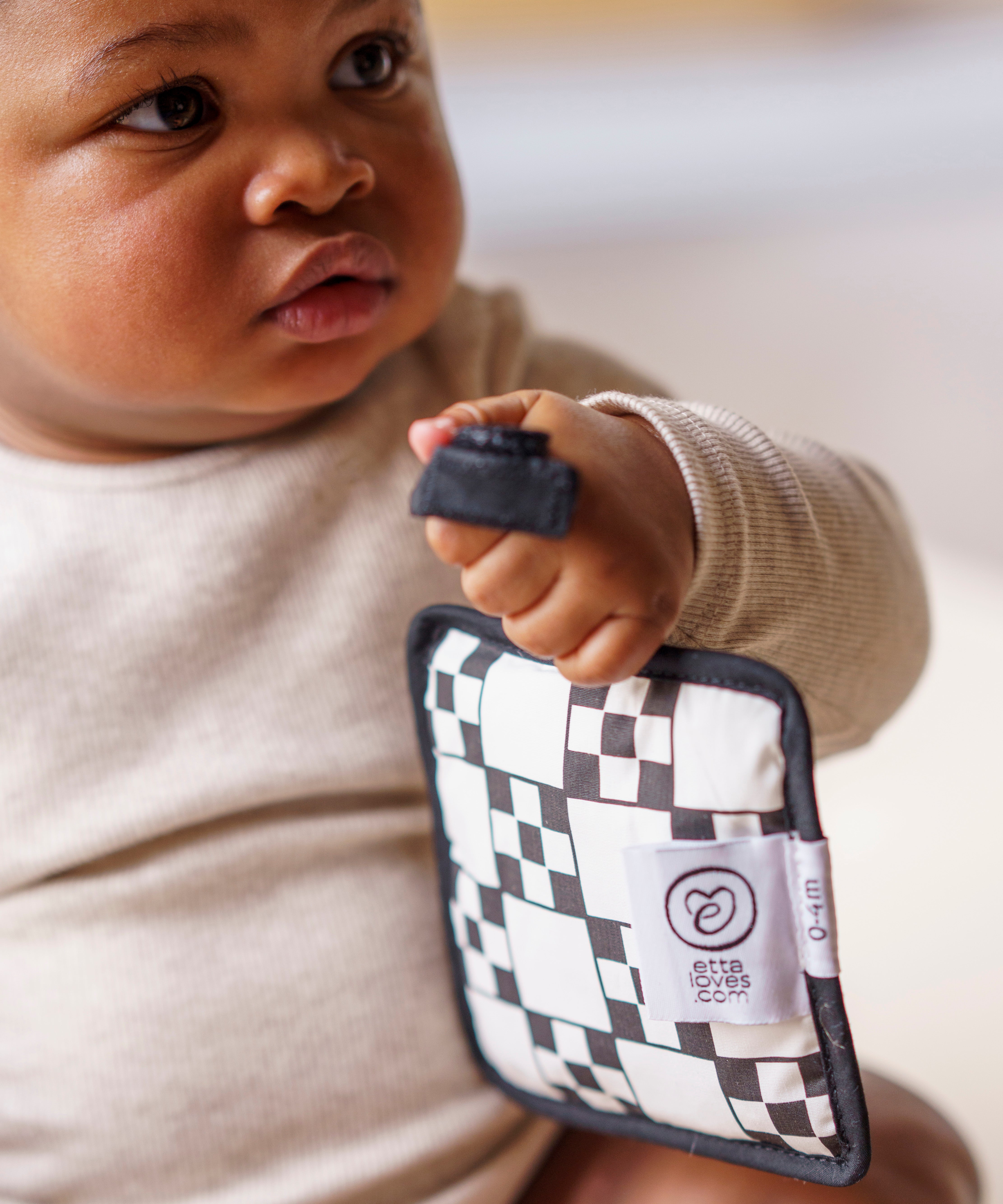 A baby holding a Etta Loves sensory hanging square on mono design to give an idea on size