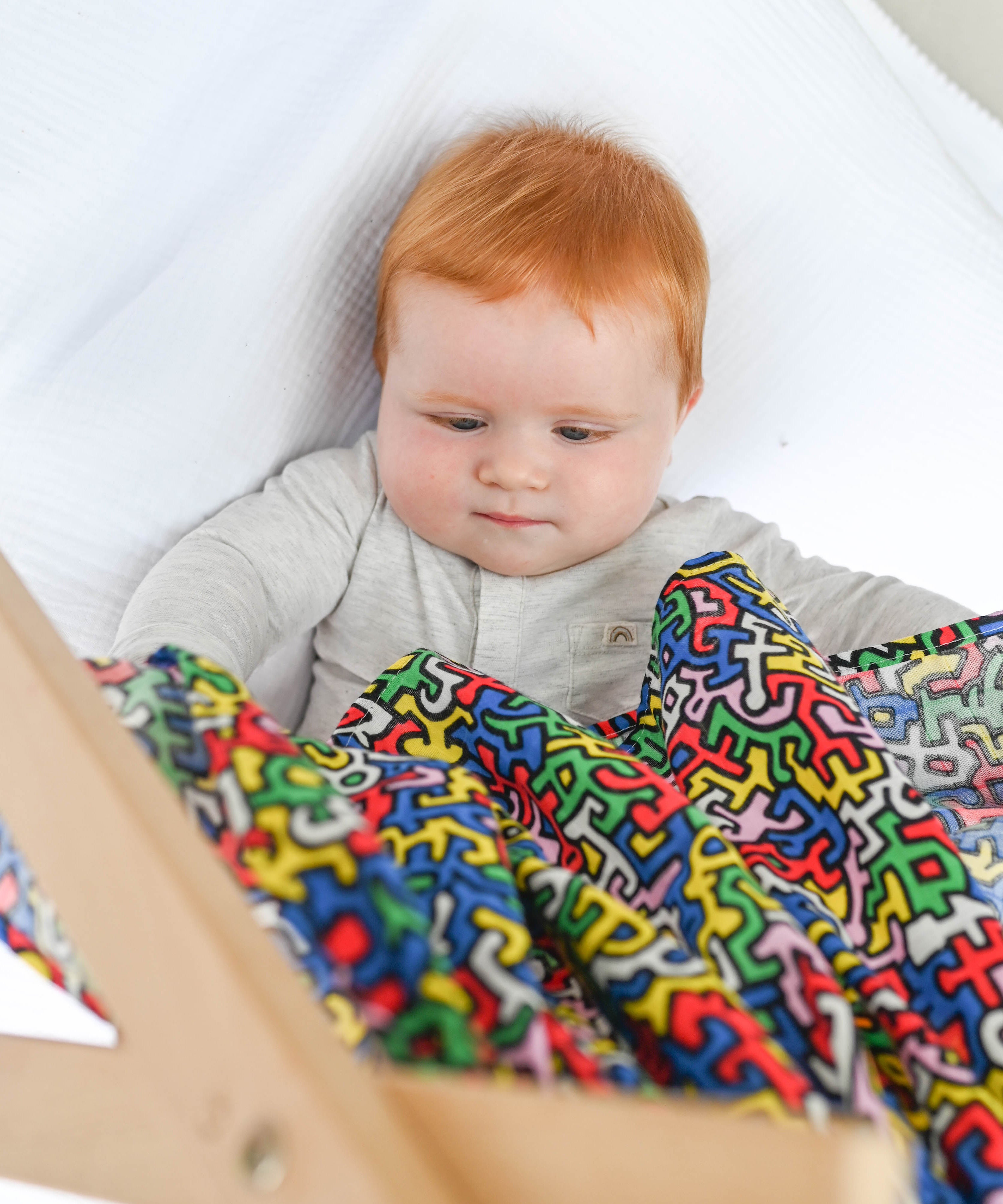 A baby holding the Etta Loves X Keith Haring Extra Large Organic Cotton Baby Muslin Square in Brazil design