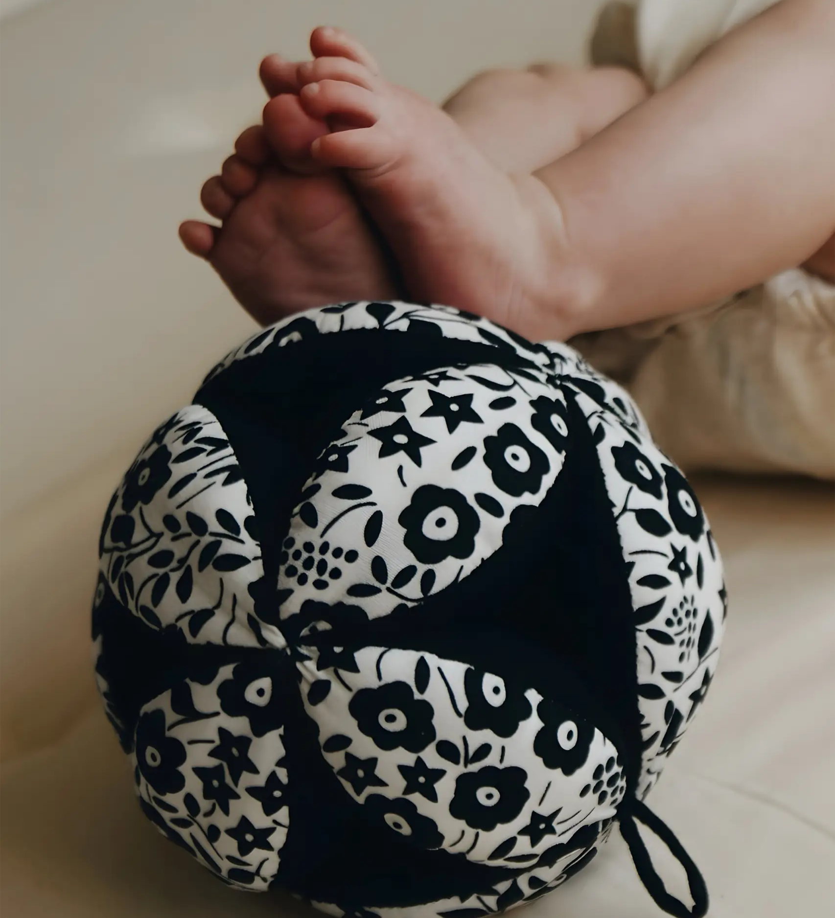 Etta Loves x Liberty organic cotton sensory grasping ball near baby feet showing scale and the Liberty pattern