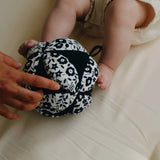 Adult holding a Etta Loves x Liberty organic cotton sensory grasping ball near baby feet 