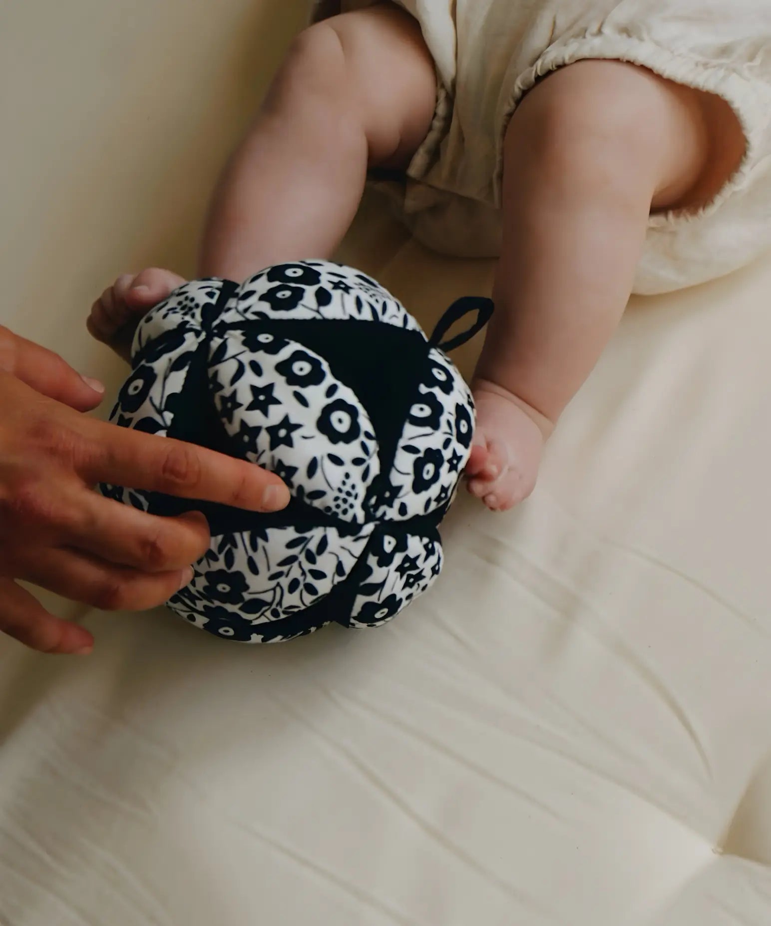 Adult holding a Etta Loves x Liberty organic cotton sensory grasping ball near baby feet 