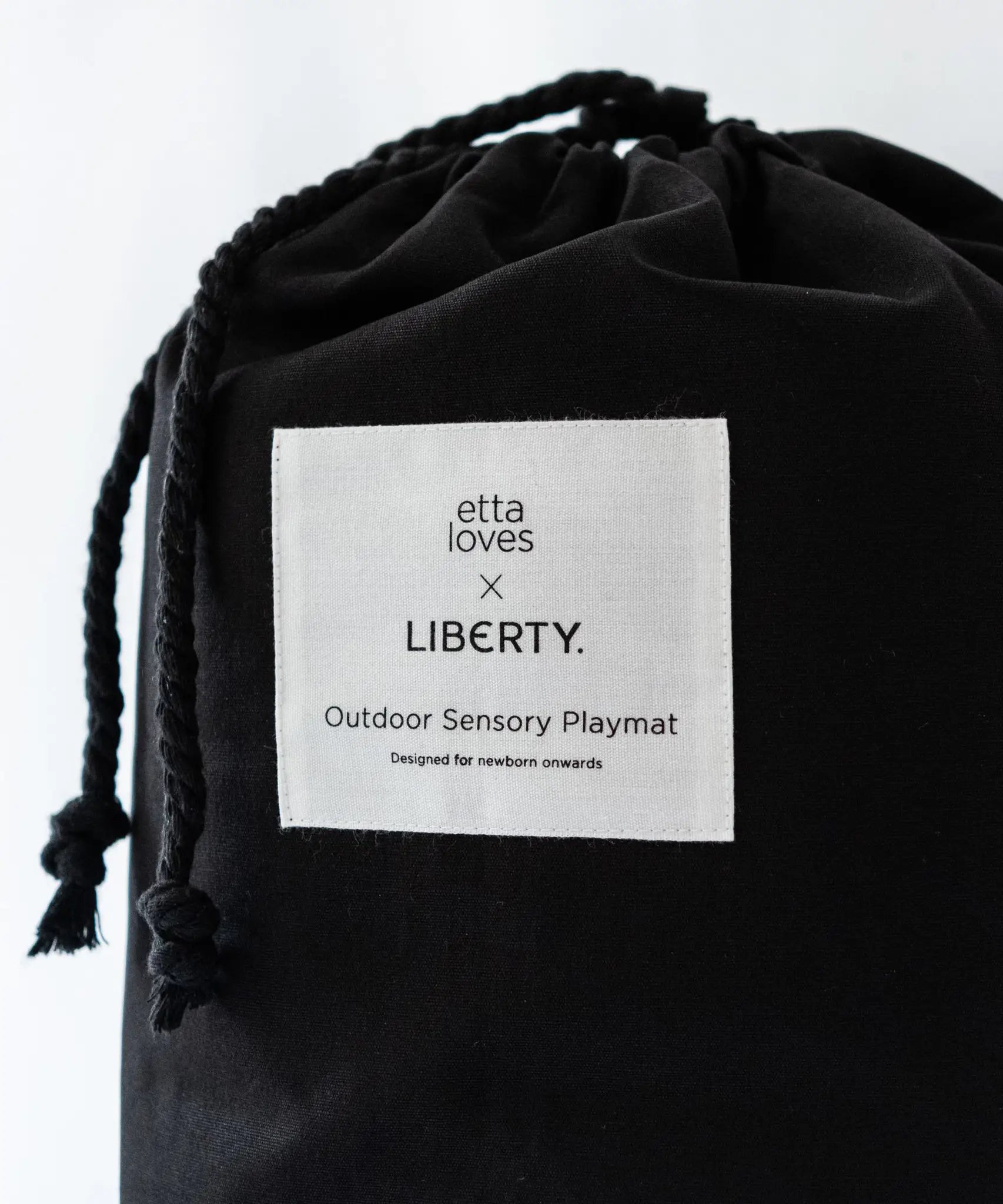 Black cotton bag with a brand patch and drawstring to hold the Etta Loves x Liberty organic cotton playmat 