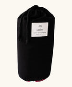 Black cotton bag with a brand patch holding the Etta Loves x Liberty organic cotton sensory colourful outdoor playmat 