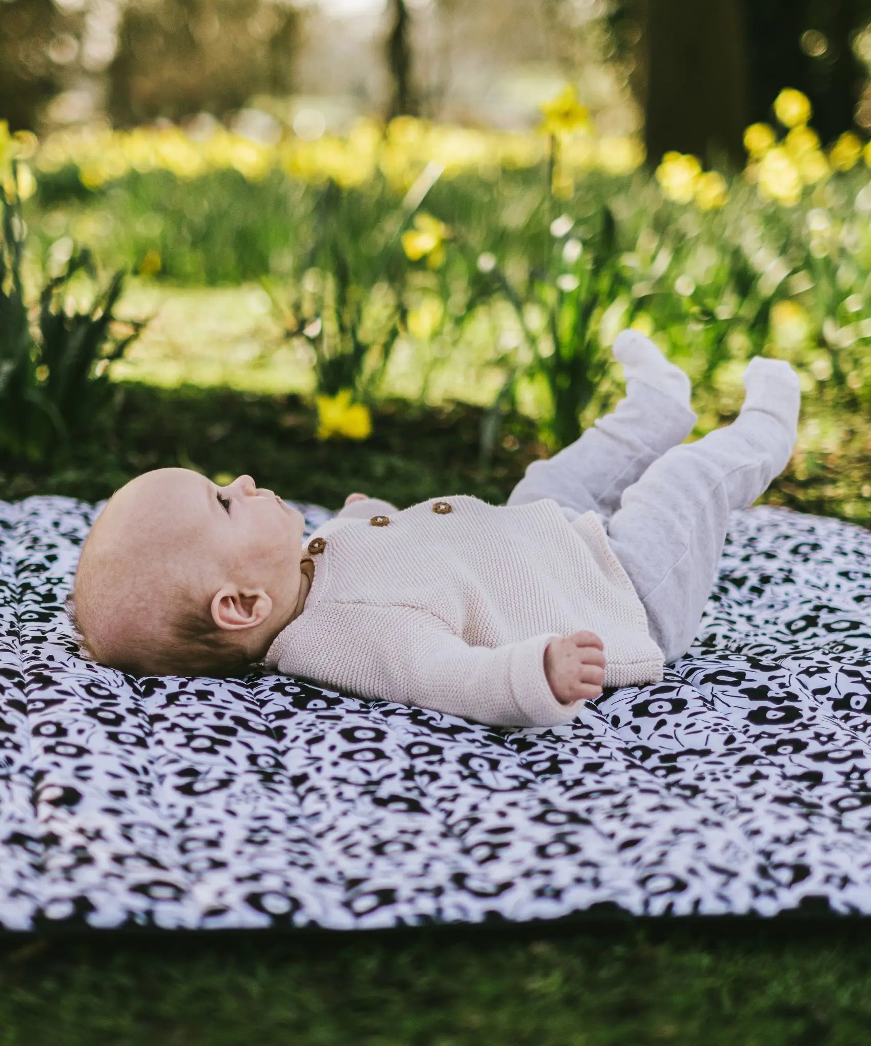 Baby lying on its back on the Etta Loves x Liberty organic cotton monochrome sensory playmat 