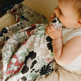 Baby with the pastel floral Etta Loves x Liberty muslin cloth in its mouth as sensory play. 