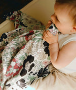 Baby with the pastel floral Etta Loves x Liberty muslin cloth in its mouth as sensory play. 