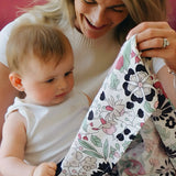 Mother holding a Etta Love x Liberty pastel floral design organic cotton muslin cloth in front of a baby. 