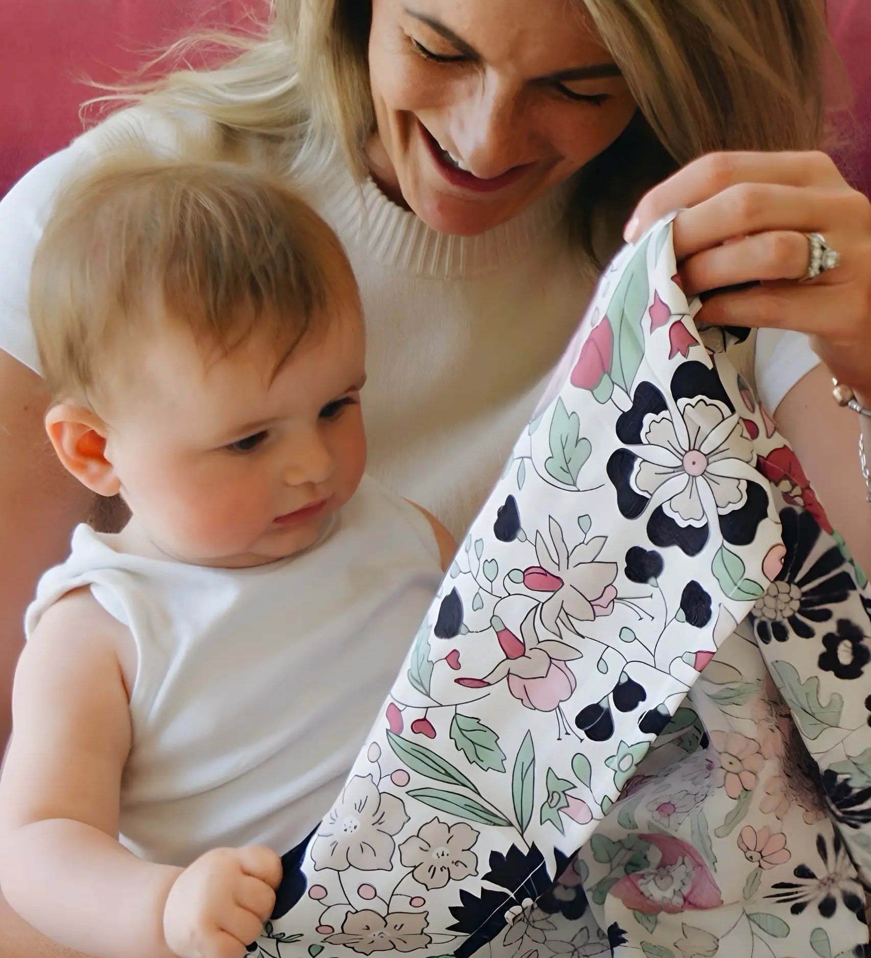 Mother holding a Etta Love x Liberty pastel floral design organic cotton muslin cloth in front of a baby. 