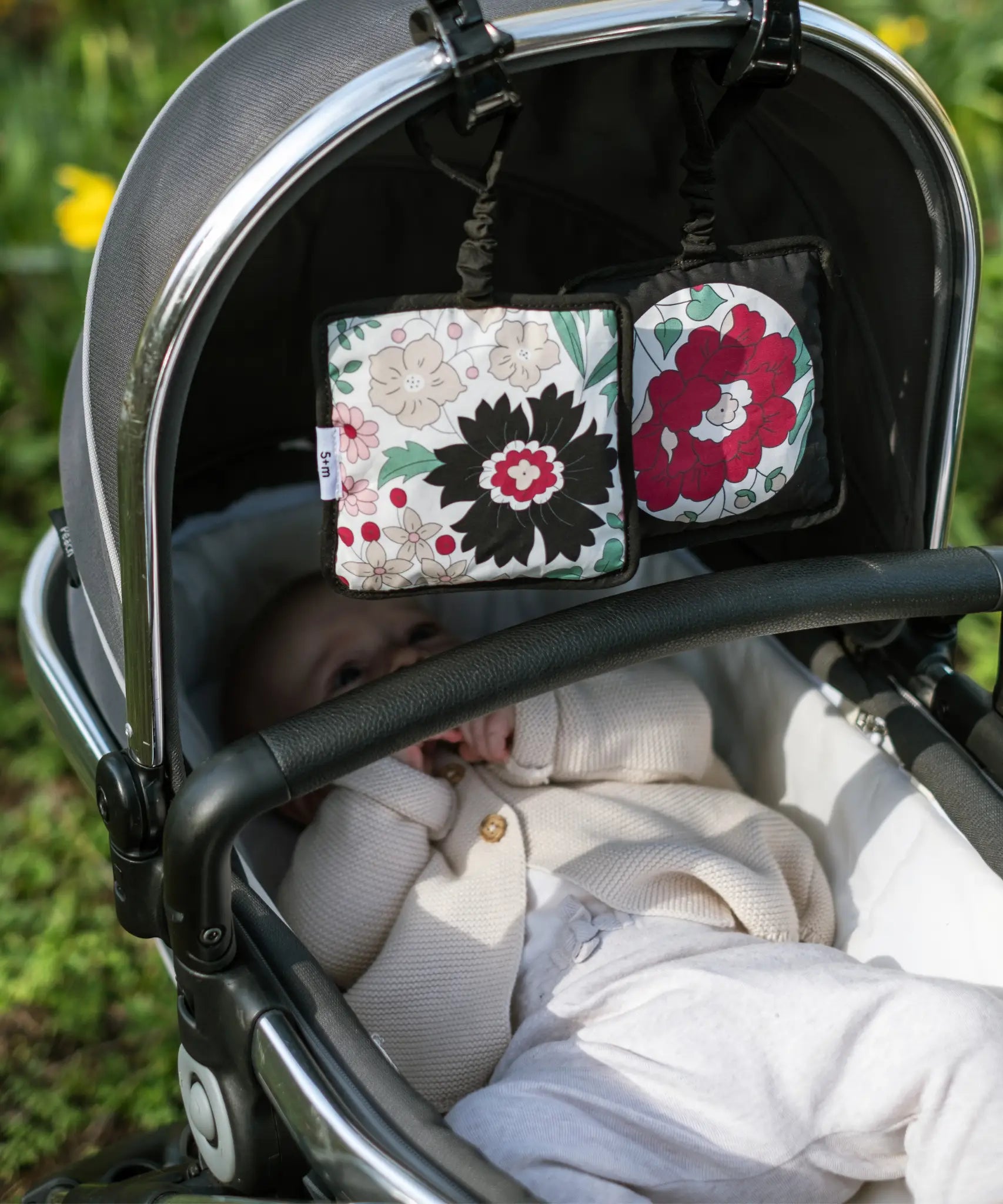 2 Etta Loves x Liberty sensory hanging squares showing the floral pastel design hanging on a buggy with a baby inside 