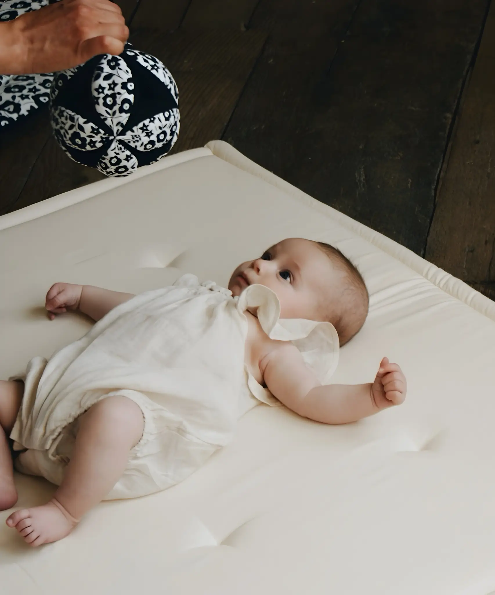 Adult holding a Etta Loves x Liberty organic cotton sensory grasping ball above a baby 