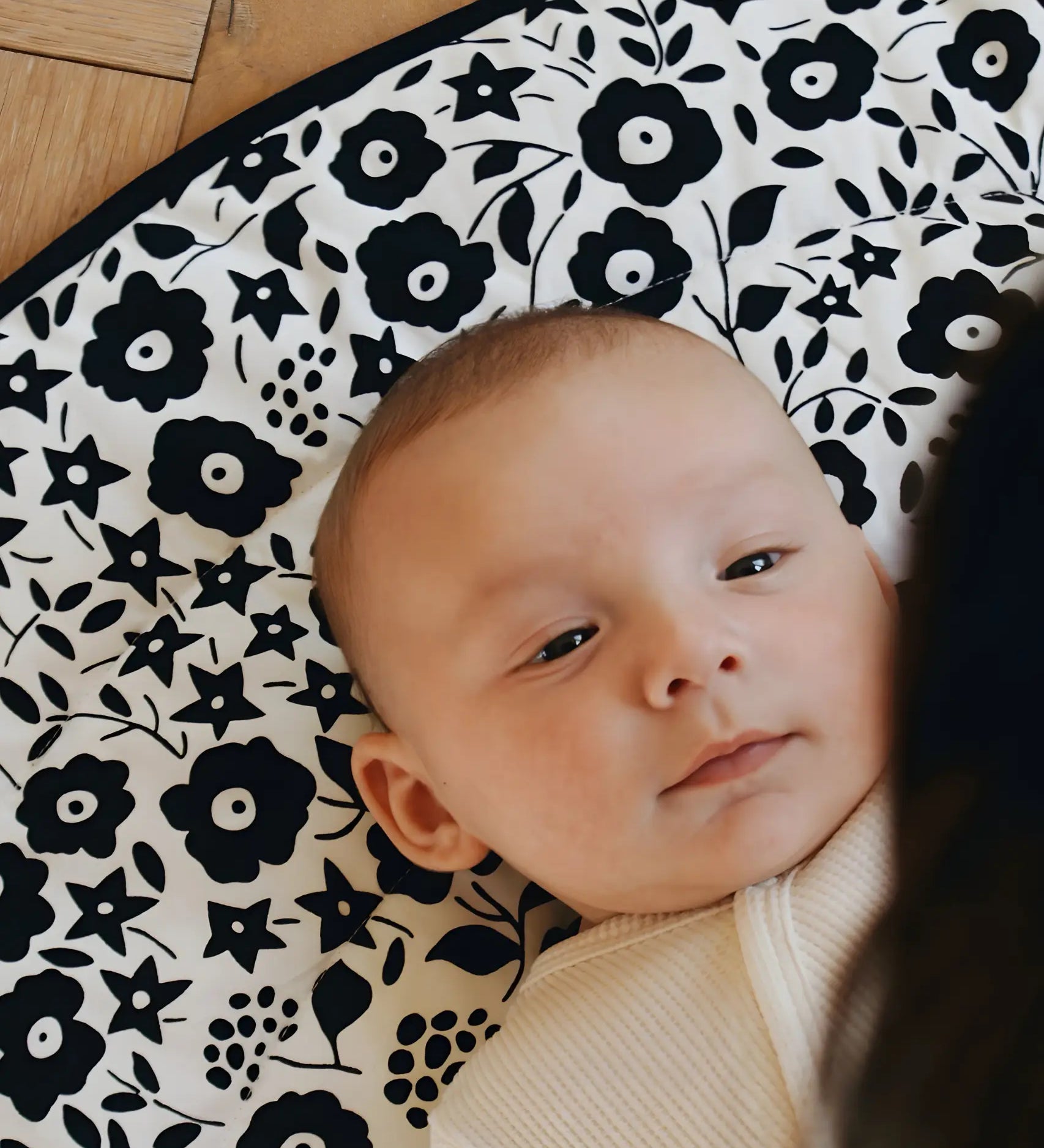 Baby lying on its back on the GOTS organic cotton Etta Loves x Liberty sensory reversible playmat showing the Fairford shadow design