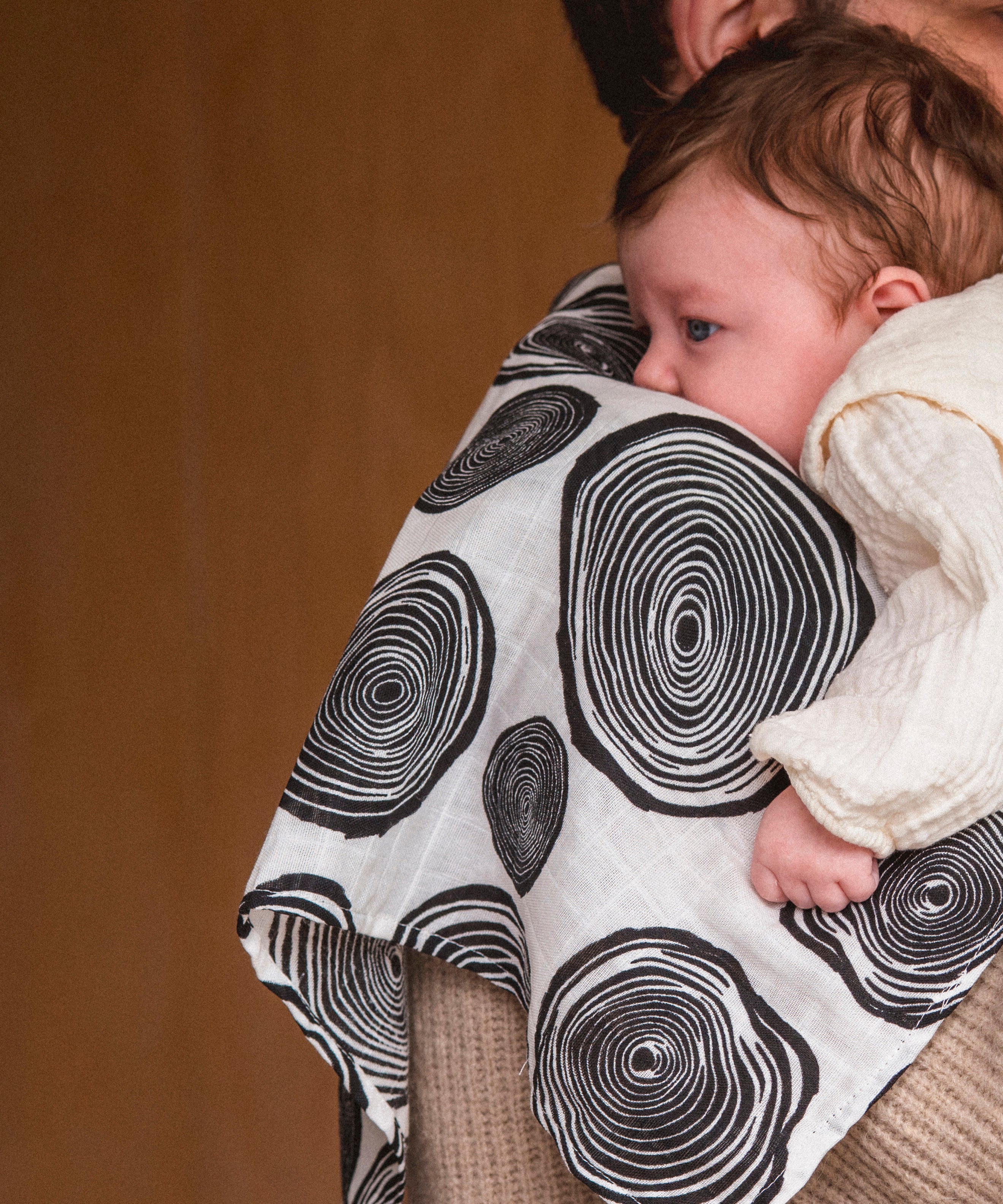 An adult holding a baby with the Etta Loves muslin square in plan print on the shoulder