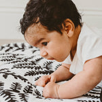A baby lying down on the Etta Loves Reversible Organic Cotton Baby Play Mat - Plant Print with black and white Ferns