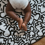 A baby lying down and looking at the 'Brazil' print on the Etta Loves X Keith Haring Reversible Organic Cotton Baby Play Mat
