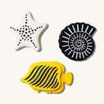 Etta Loves Natural Rubber Animal Sensory Bath Toys - 3 Pack which includes a white starfish with black spots, a black seashell with white lines, and a yellow fish with black stripes and one blue stripe, on a cream background